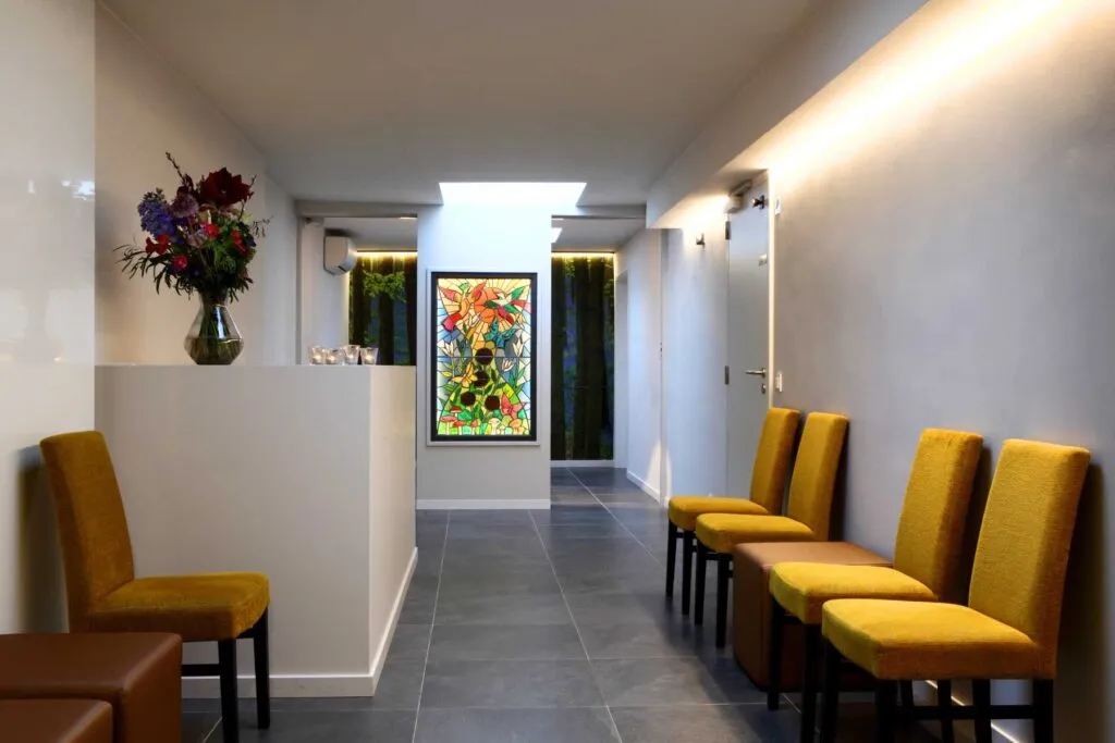 Van Kuyk Uitvaartcentrum Merksem — wachtruimte met gele zetels en kunstwerk